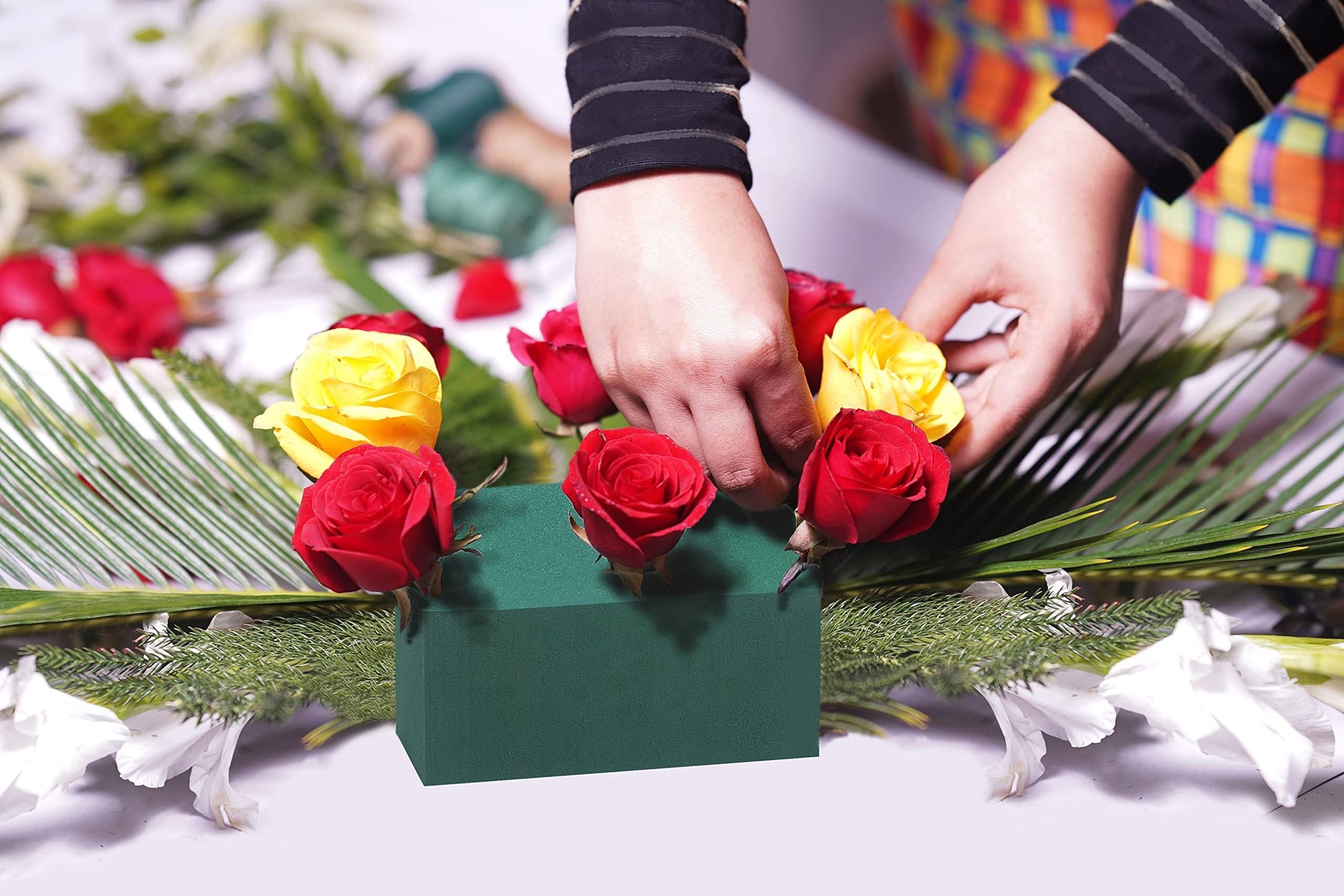 Hands arranging red and yellow roses into a green floral foam block for a flower arrangement.