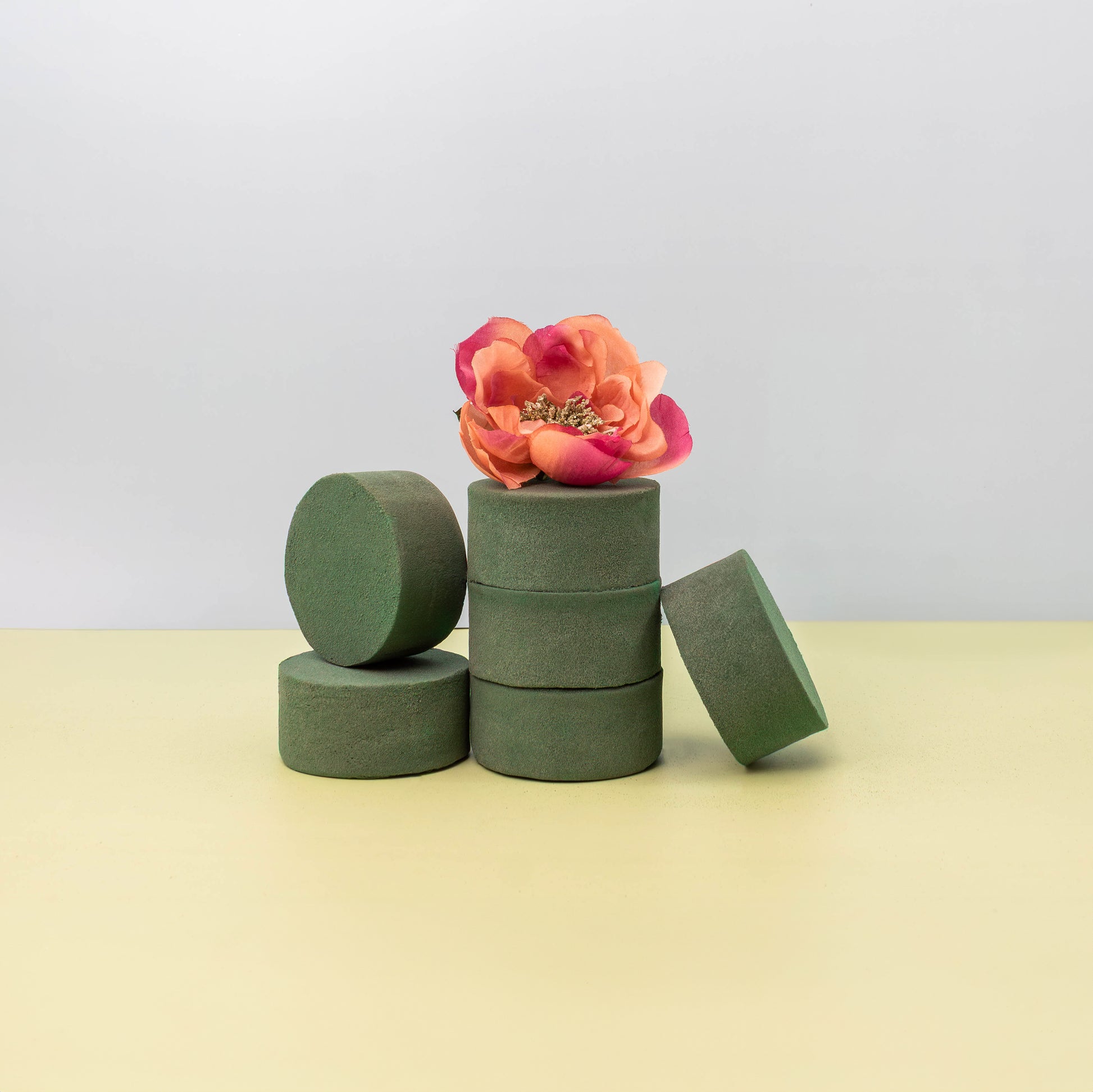 Green floral foam blocks stacked with a bouquet of artificial pink peony and yellow hydrangea flowers on a light background