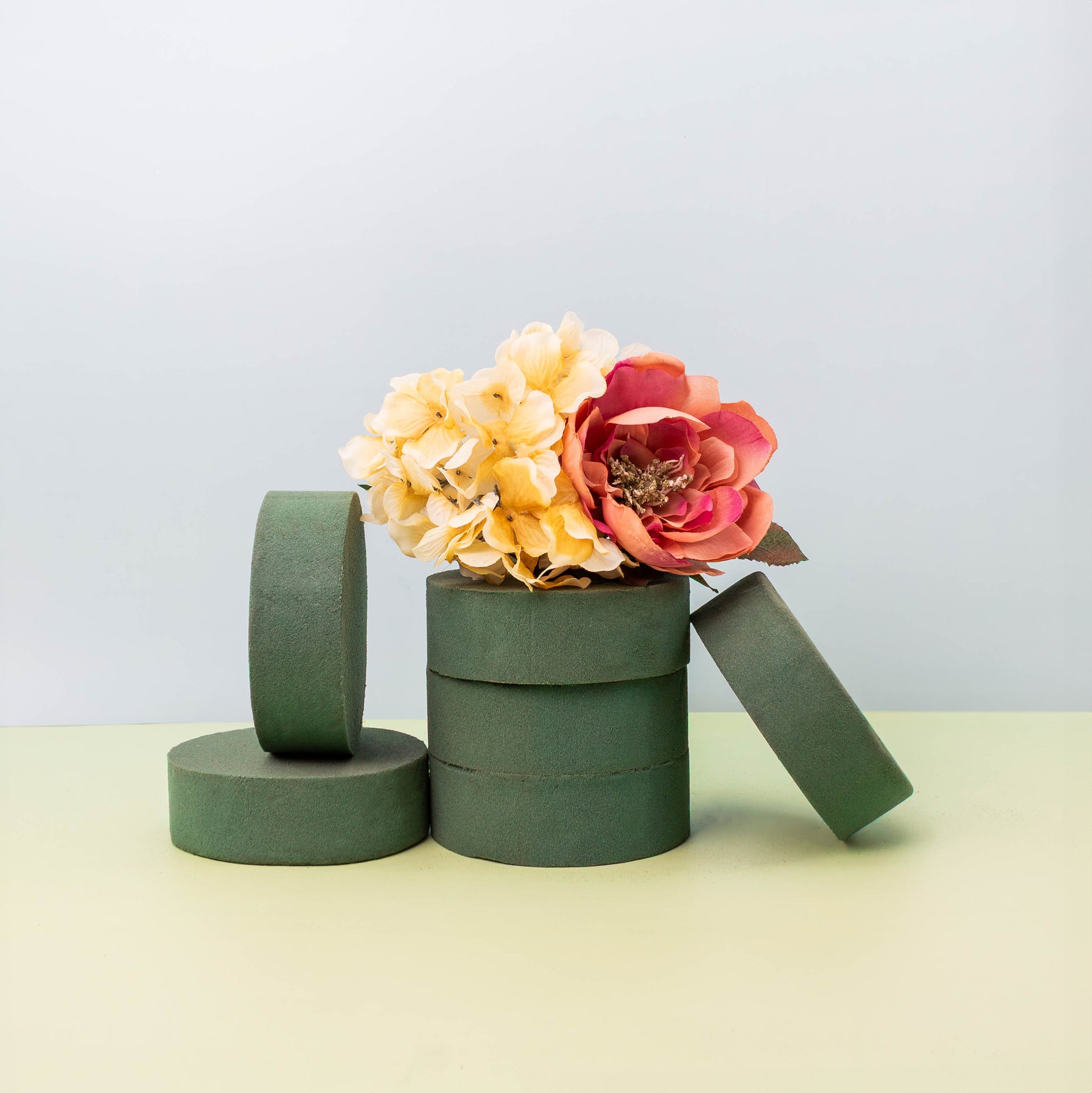 Green floral foam blocks stacked with a bouquet of artificial pink peony and yellow hydrangea flowers on a light background