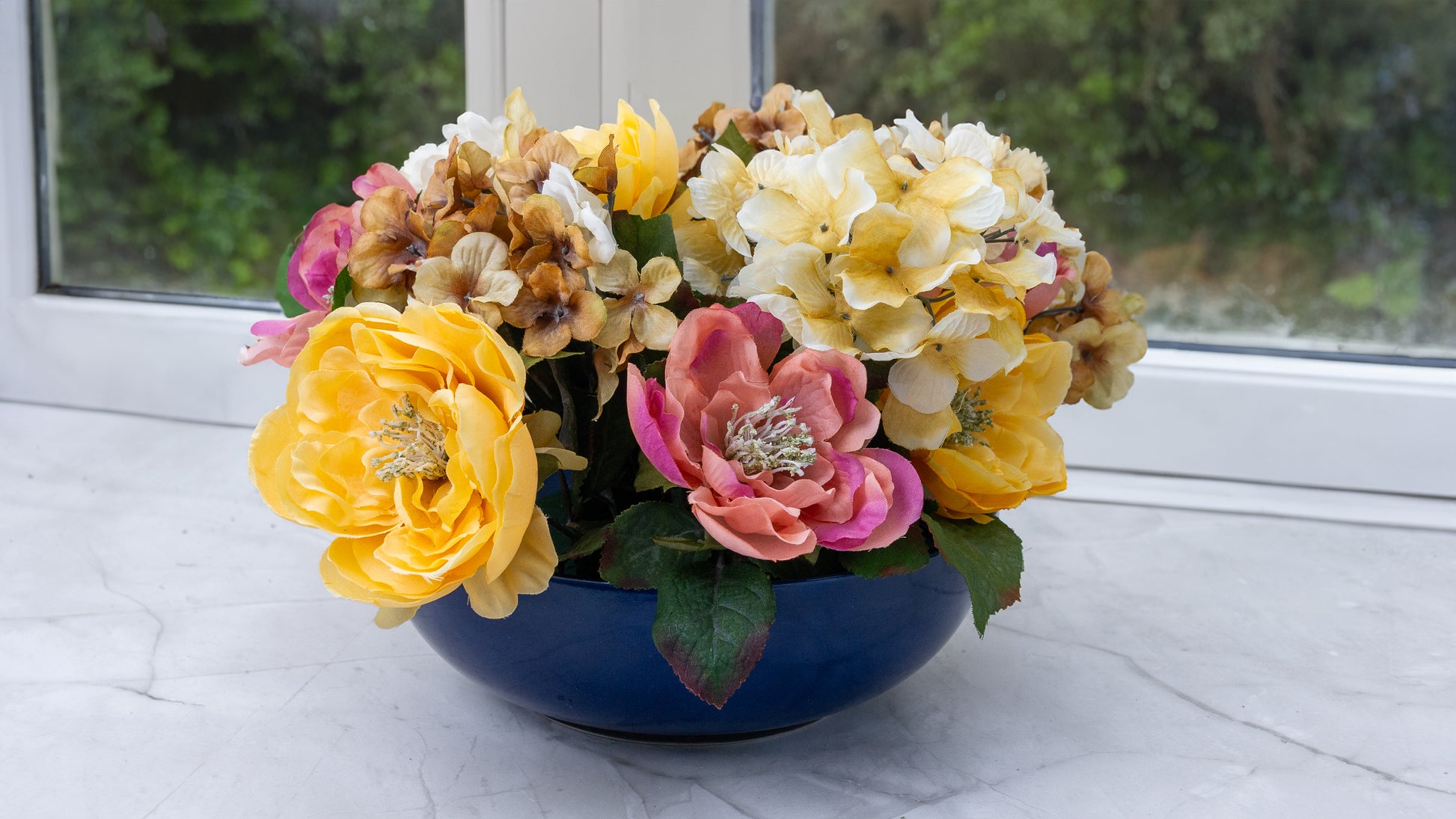 Green floral foam brick soaking in a clear bowl of water, surrounded by various fresh flowers, ready for flower arrangement.
