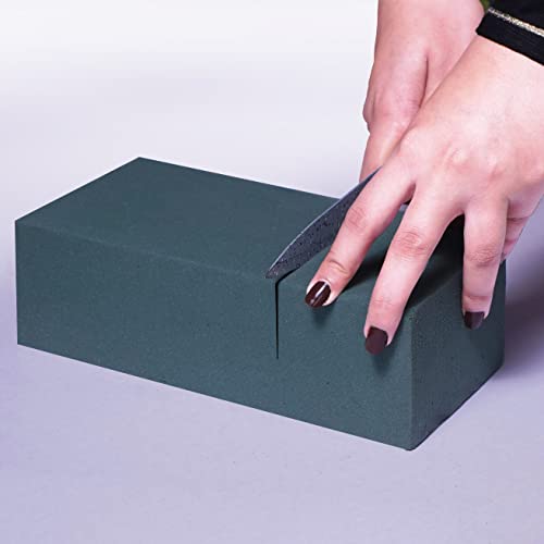 A person's hands using a knife to cut a rectangular block of green floral foam.