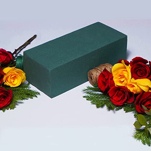 A green rectangular floral foam block is centered, surrounded by red and yellow roses and green foliage on a white surface.