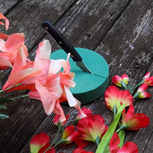 Floral foam block with a knife, surrounded by pink and red flowers, all resting on a rustic wooden surface.
