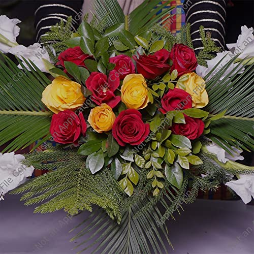 A vibrant floral arrangement featuring red and yellow roses, white lilies, and various green foliage including palm leaves and cypress branches.