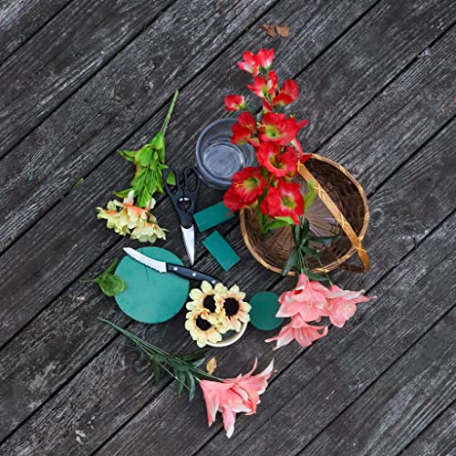 Floral arrangement supplies including red, pink, and yellow flowers, green floral foam, basket, scissors, and knife on wood.
